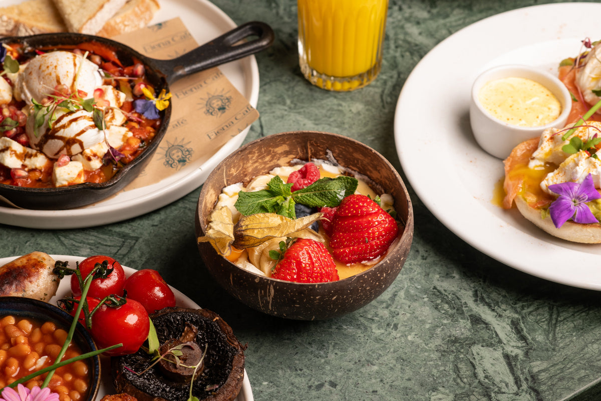 Breakfast at Fiena on green marble: an egg skillet, a granola and fruit bowl, eggs Benedict and fresh orange juice