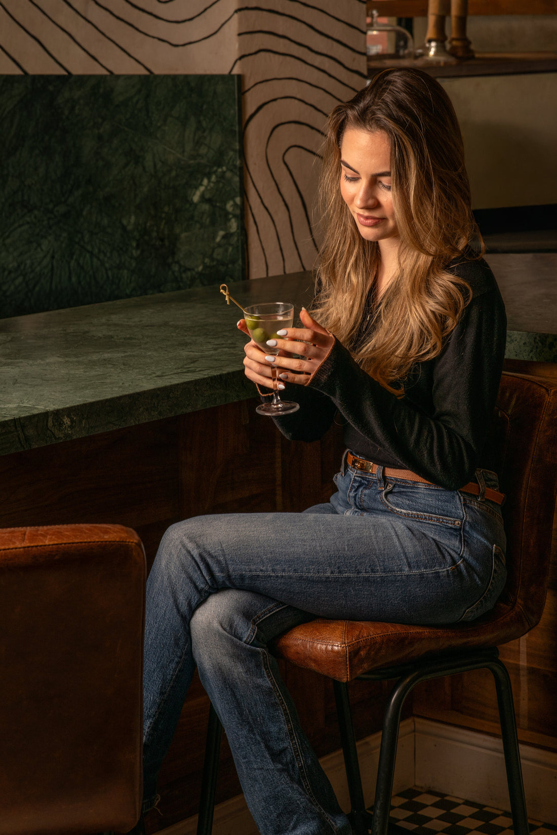 A guest with a cocktail at Fiena's green marble bar, on a leather bar stool