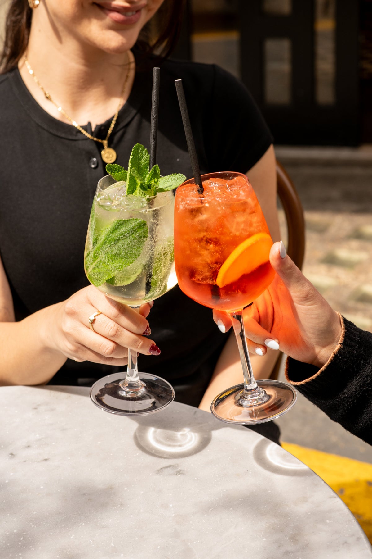 Two spritzes raised in a toast over a marble table at Fiena