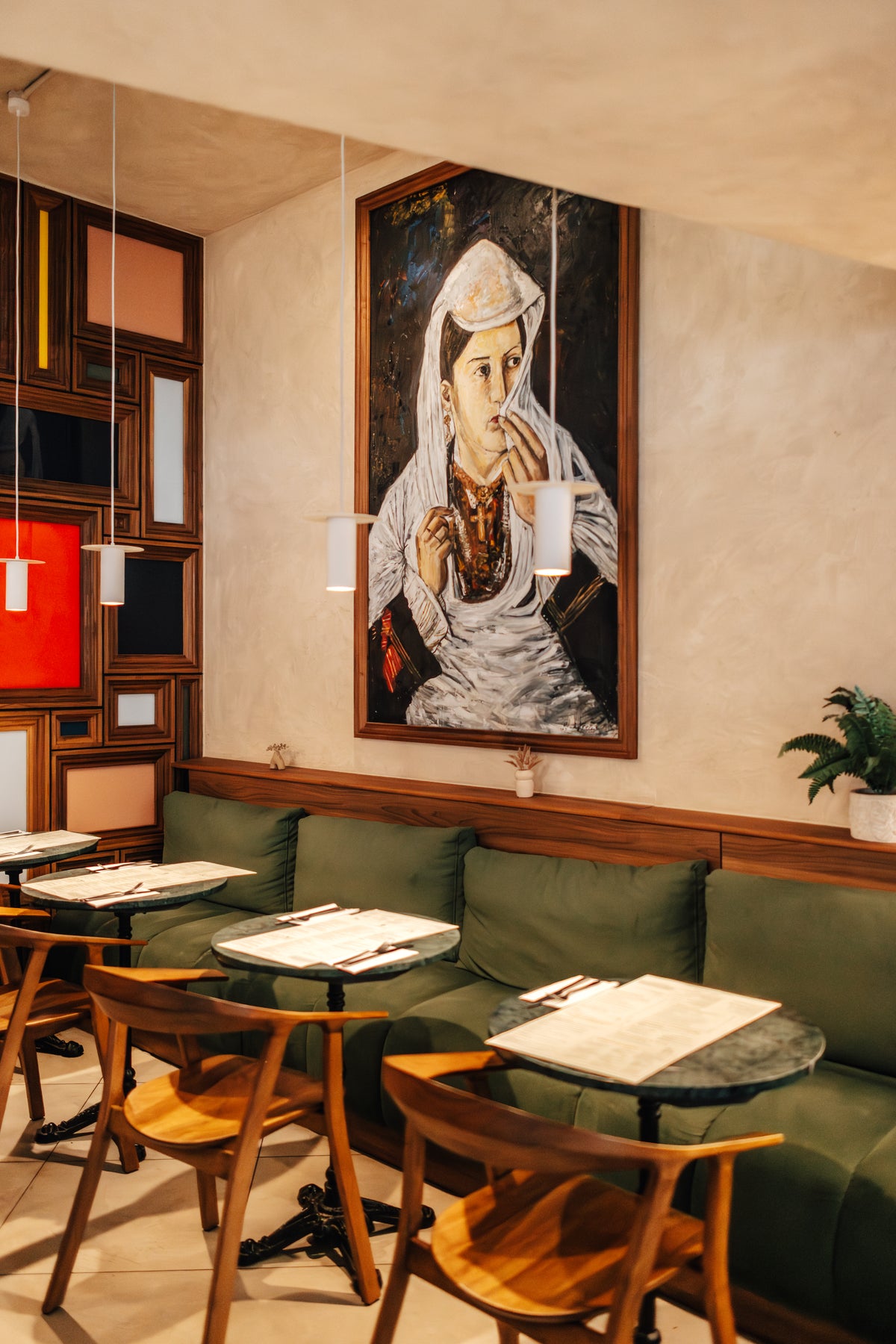 The dining room at Fiena, King's Cross, with green banquettes and a large portrait painting